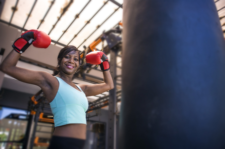 lifestyle indoors gym portrait of young attractive and beautiful black afro American woman training happy posing playful wearing boxing gloves at modern and cool combat fitness clubの写真素材