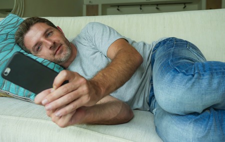 lifestyle indoors portrait of young happy and attractive man at home sofa couch using internet...