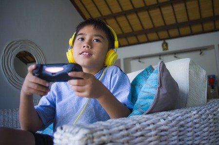 lifestyle portrait of Latin little kid excited and happy playing video game online with headphones...