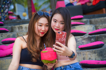 lifestyle outdoors portrait of young happy and beautiful Asian Chinese girls taking selfie picture...