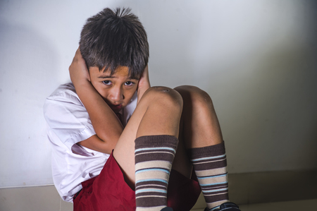 lifestyle dramatic bullying victim portrait of young sad and scared kid 7 - 10 years old in school uniform sitting alone crying depressed and frightened suffering abuse problem helpless and bulliedの写真素材