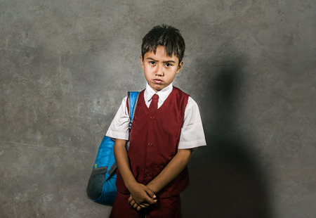 young bullied and abused schoolboy in uniform carrying school bag sad and depressed on blackboard feeling a lonely and stressed kid victim of bullying in child depression conceptの写真素材