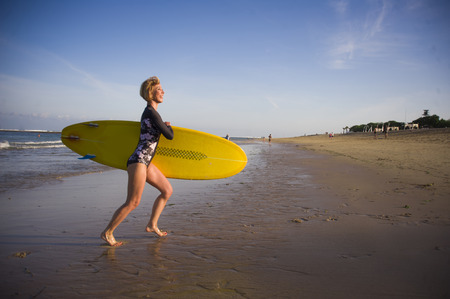 young attractive and happy blonde surfer girl in beautiful beach carrying yellow surf board running...