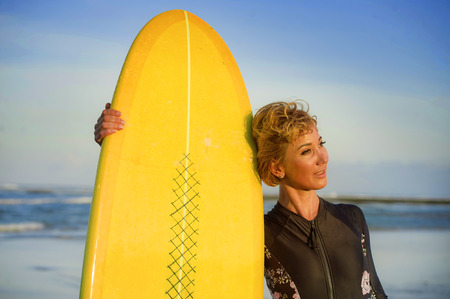 lifestyle portrait of young sexy beautiful and happy surfer woman holding yellow surf board smiling...