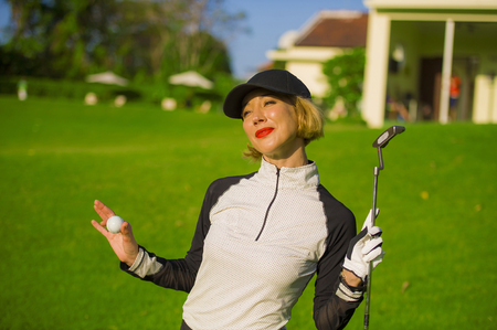 lifestyle outdoors portrait of young beautiful and happy woman at playing golf holding ball and putter club smiling cheerful in stylish golfing clothes isolated on green put backgroundの写真素材