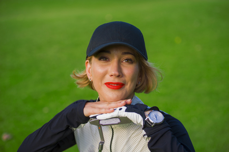 lifestyle outdoors portrait of young beautiful and happy woman at playing golf leaning sweet on club smiling cheerful in stylish golfing clothes isolated on green put backgroundの写真素材