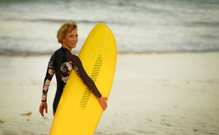 young beautiful and happy surfer girl walking towards the sea carrying yellow surf board ready for surfing smiling cheerful enjoying summer holidays at beautiful tropical beachの写真素材