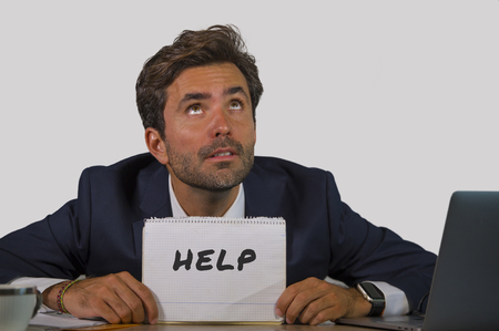young attractive sad and depressed business man working at office laptop computer desk holding notepad asking for help feeling desperate overwhelmed and exhausted in corporate job lifestyleの写真素材