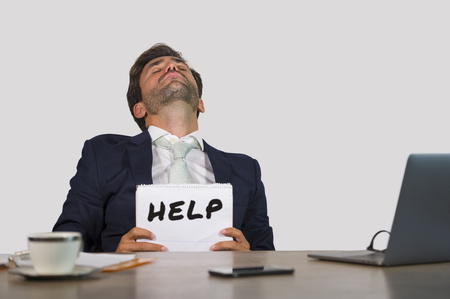 young attractive sad and depressed business man working at office laptop computer desk holding notepad asking for help feeling desperate overwhelmed and exhausted in corporate job lifestyleの写真素材