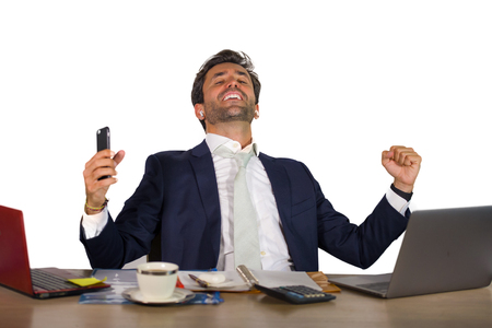 young happy and successful handsome businessman in suit working at office computer desk celebrating financial success winning money smiling cheerful and satisfied in business lifestyle conceptの写真素材