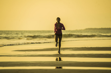 young happy and attractive African American runner woman exercising on running workout at beautiful beach jogging and enjoying sunset in health care fitness and outdoors activity conceptの写真素材