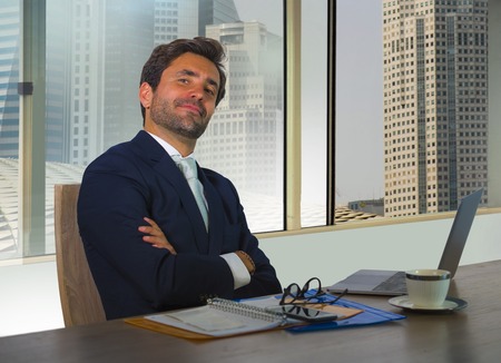 corporate portrait of young happy handsome and attractive businessman working at computer desk in modern office at central business financial district smiling satisfied feeling successfulの写真素材