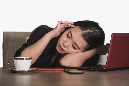 young beautiful sad and depressed Asian Chinese business woman working in stress at office computer desk feeling overwhelmed and frustrated suffering headache and depression isolatedの写真素材