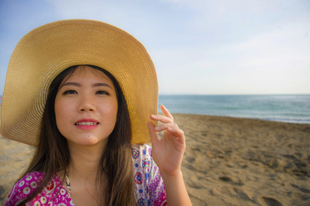 close up lifestyle portrait of young beautiful and happy Asian Korean tourist woman in Summer hat smiling cheerful at tropical island beach looking at the camera enjoying Summer holidays travelの写真素材