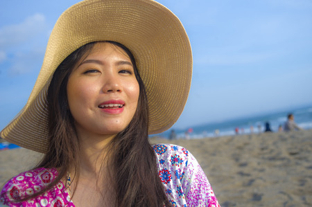 close up lifestyle portrait of young beautiful and happy Asian Chinese tourist woman in Summer hat smiling cheerful at tropical island beach looking at the camera enjoying Summer holidays travelの写真素材