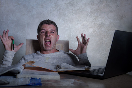 young worried and desperate man working late night at home desk with laptop computer screaming...