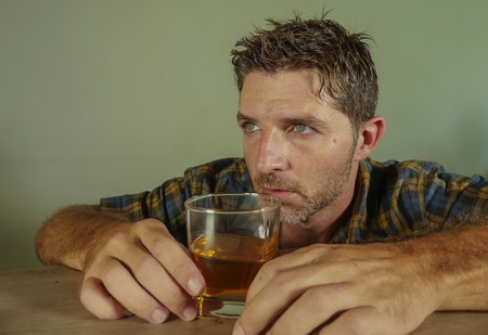 young attractive wasted and depressed addict and alcoholic man with whiskey glass thoughtful and sad...