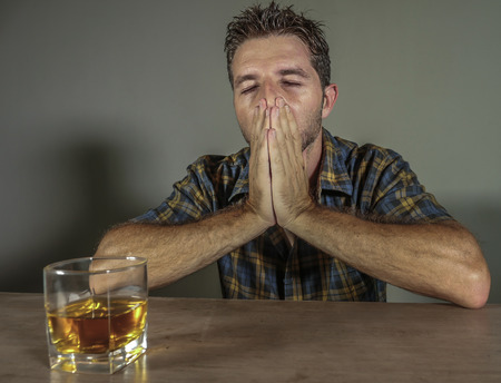 isolated portrait of young drunk addict and alcoholic man drinking whiskey glass intoxicated looking...
