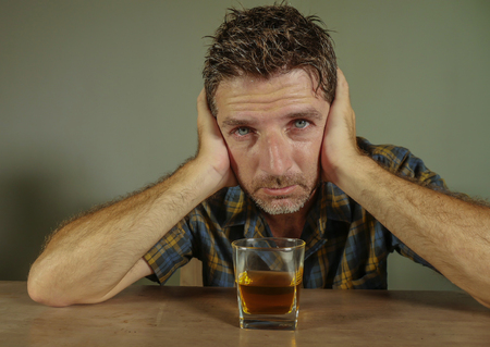 isolated portrait of young drunk addict and alcoholic man drinking whiskey glass intoxicated looking...