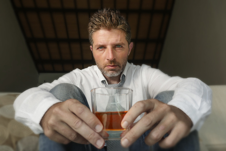 young attractive sad and desperate drunk addict businessman at home sofa couch drinking holding...