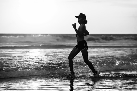 silhouette of fit and athletic Asian Chinese sporty woman running on beautiful beach doing jogging workout on sunset in fitness healthy lifestyle and summer outdoors activity conceptの写真素材