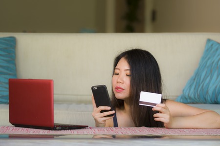 young happy and beautiful Asian Chinese woman holding credit card using mobile phone for internet banking and online shopping smiling in finance success and electronic business conceptの写真素材