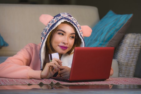 young happy and beautiful girl in winter hoodie buying on internet paying with credit card online shopping Christmas present smiling cheerful and excited  in e-commerce xmas gift conceptの写真素材