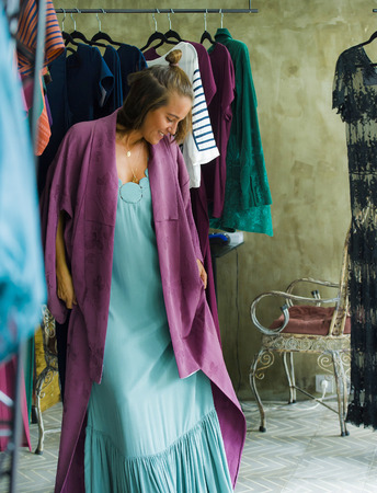 young beautiful and happy blond woman enjoying shopping trying out clothes in the mirror at vintage and cool beauty fashion store smiling cheerful having fun buying sales and opportunity clothingの写真素材