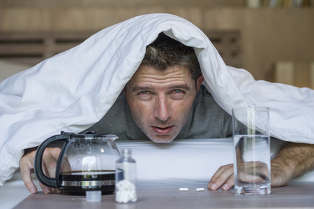 lifestyle home portrait of young exhausted and wasted man waking up suffering headache and hangover after drinking alcohol at night party lying on bed sick and miserable still drunkの写真素材