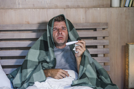 young sick wasted and exhausted man at home bed lying feeling unwell suffering cold and flu sneezing nose with tissues having virus and headache in domestic health care and grippe conceptの写真素材