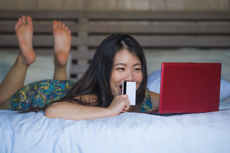 young beautiful and happy Asian Chinese woman using credit card internet banking on laptop computer...