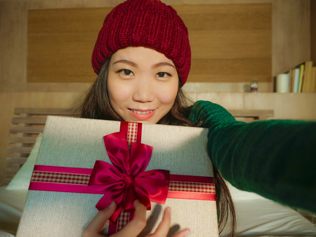 young beautiful and happy Asian Chinese girl taking selfie picture with mobile phone holding...