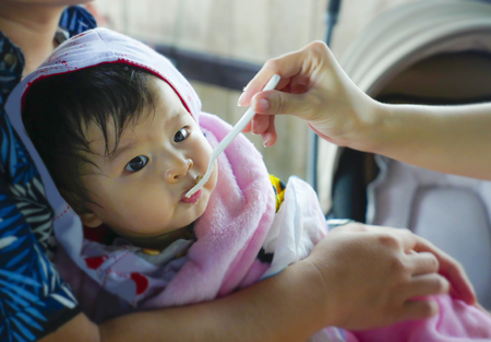 woman hand with spoon feeding her daughter , a sweet and adorable beautiful Asian Chinese baby girl hold by her father having her meal in healthy nutrition and young family lifestyle conceptの写真素材