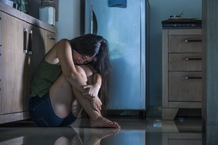 young desperate and depressed Asian Chinese woman crying scared at home kitchen floor feeling anxious and sad suffering depression and anxiety victim of domestic violence and husband abuseの写真素材