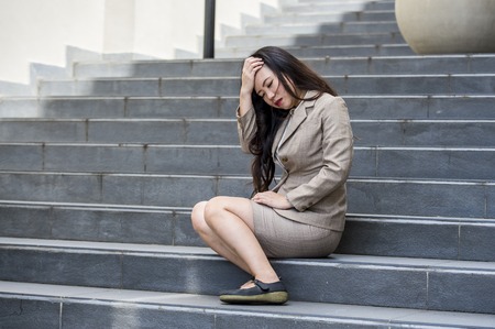 young depressed and desperate Asian Korean businesswoman crying alone sitting on street staircase suffering stress and depression crisis being victim of mobbing or fired losing her jobの写真素材