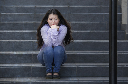 young sad and depressed Asian Japanese student woman or bullied teenager sitting outdoors on street staircase overwhelmed and anxious feeling desperate suffering depression problemの写真素材