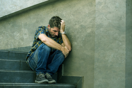 young sad and desperate man sitting outdoors at street stairs suffering anxiety and depression...