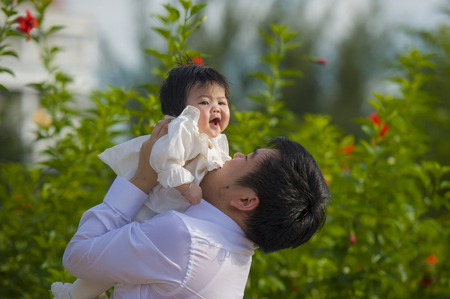 young happy and proud man as father of sweet little baby girl holding her daughter in front of flowers garden at holidays resort enjoying together outdoors in family lifestyle conceptの写真素材