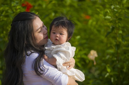 young happy and cute Asian Chinese woman enjoying and playing with her baby girl daughter holding...