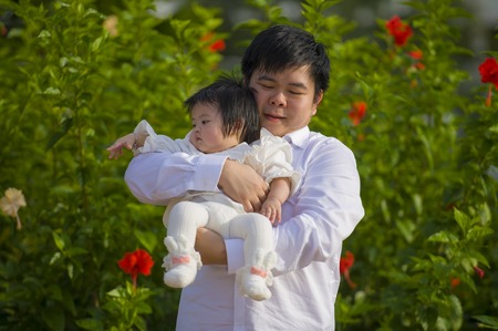 young happy and proud man as father of sweet little baby girl holding her daughter in front of...