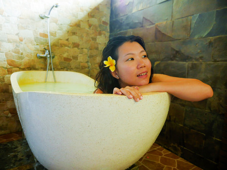 young beautiful and happy relaxed Asian Chinese woman enjoying indulging milk bath in bathtub at...