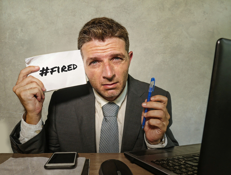 young depressed and frustrated businessman desperate at office computer desk holding notepad with...