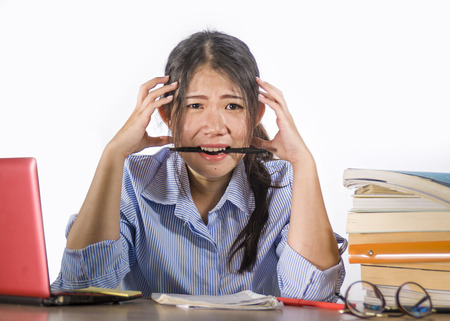 young depressed and stressed Asian Chinese student girl working with laptop and book pile overwhelmed and frustrated preparing exam feeling lazy and tired isolated on white backgroundの写真素材