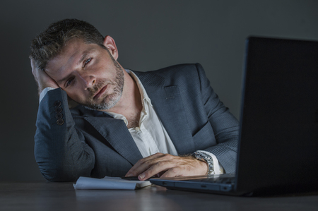 young attractive wasted and tired entrepreneur man working late night at office laptop computer desk exhausted and sleepy in financial business problem and overworked employee conceptの写真素材