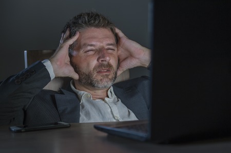 young desperate and stressed businessman working overtime at office laptop computer desk feeling anxious and overwhelmed suffering depression problem and anxiety crisis in business problemの写真素材