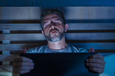 young aroused man alone in bed playing cybersex using laptop computer watching porn sex movie late at night with lascivious pervert face expression in internet pornographic sexual contentの写真素材