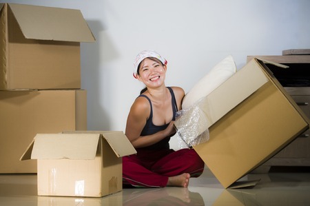 young beautiful and happy Asian Korean woman excited at home living room floor unpacking belongings...