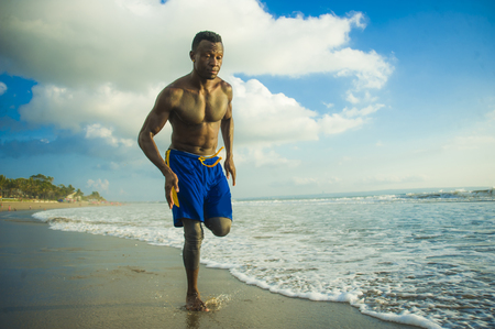 young attractive fit athletic and strong black African American man running at the beach training hard and sprinting on sea water in professional athlete lifestyle and ripped runner workoutの写真素材