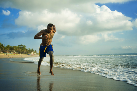 young attractive fit athletic and strong black African American man running at the beach training hard and sprinting on sea water in professional athlete lifestyle and ripped runner workoutの写真素材