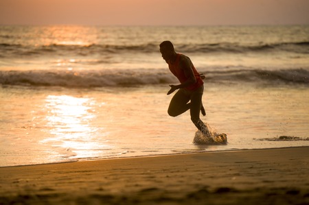 silhouette of young attractive fit athletic and strong black African American man running at sunset beach training hard and sprinting on sea water in professional athlete and runner workout